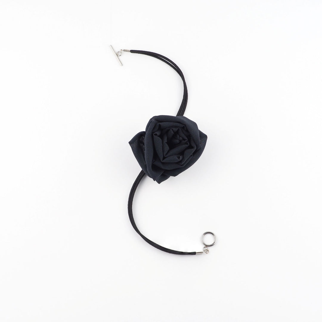 Black silk chiffon rose choker necklace with toggle clasp, arranged in a curved flat lay on a white background.