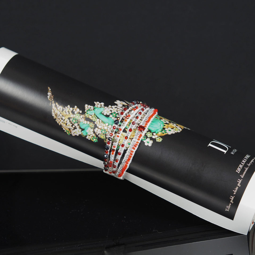 Red and white multi-strand beaded bracelet displayed wrapped around a fashion magazine, handmade on a textile base with glass beads and rhinestone detail