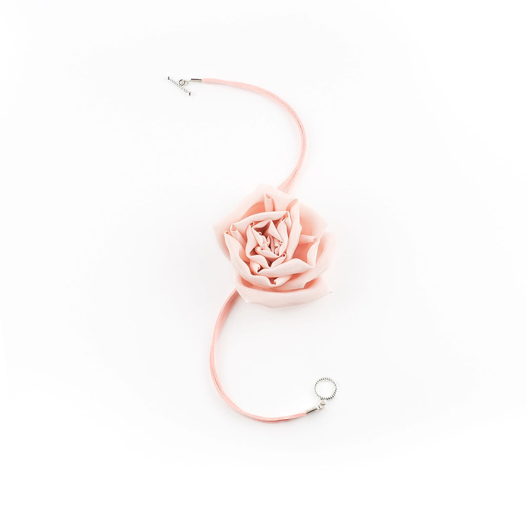 Flat lay of pink silk rose choker necklace with suede lace and toggle clasp, featuring a handmade chiffon flower