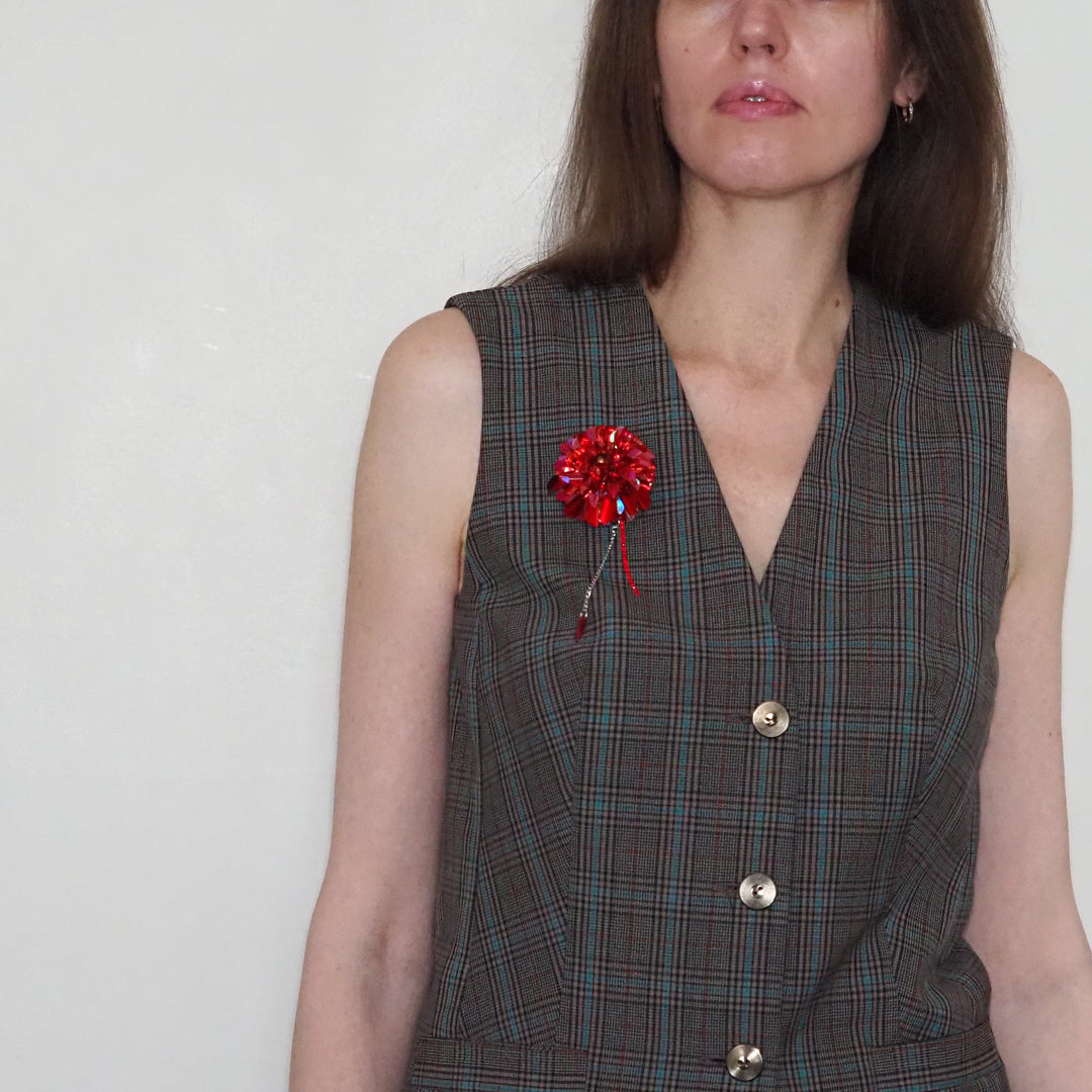 Model wearing the handcrafted red dahlia brooch on a tailored grey vest, showing how the limited edition jewelry can be styled