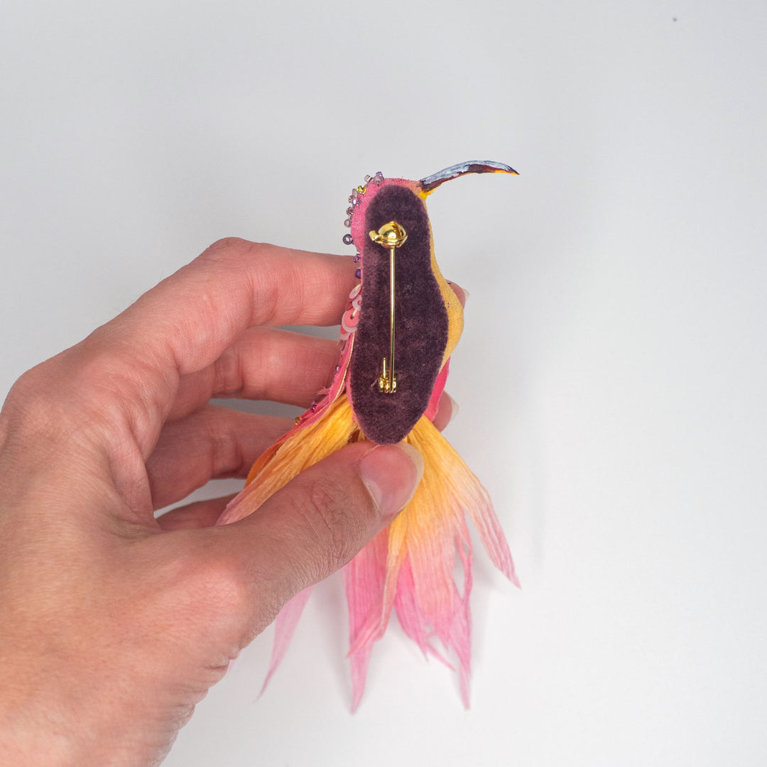 Backside of the hummingbird brooch with visible gold-tone pin fastening and dark felt backing