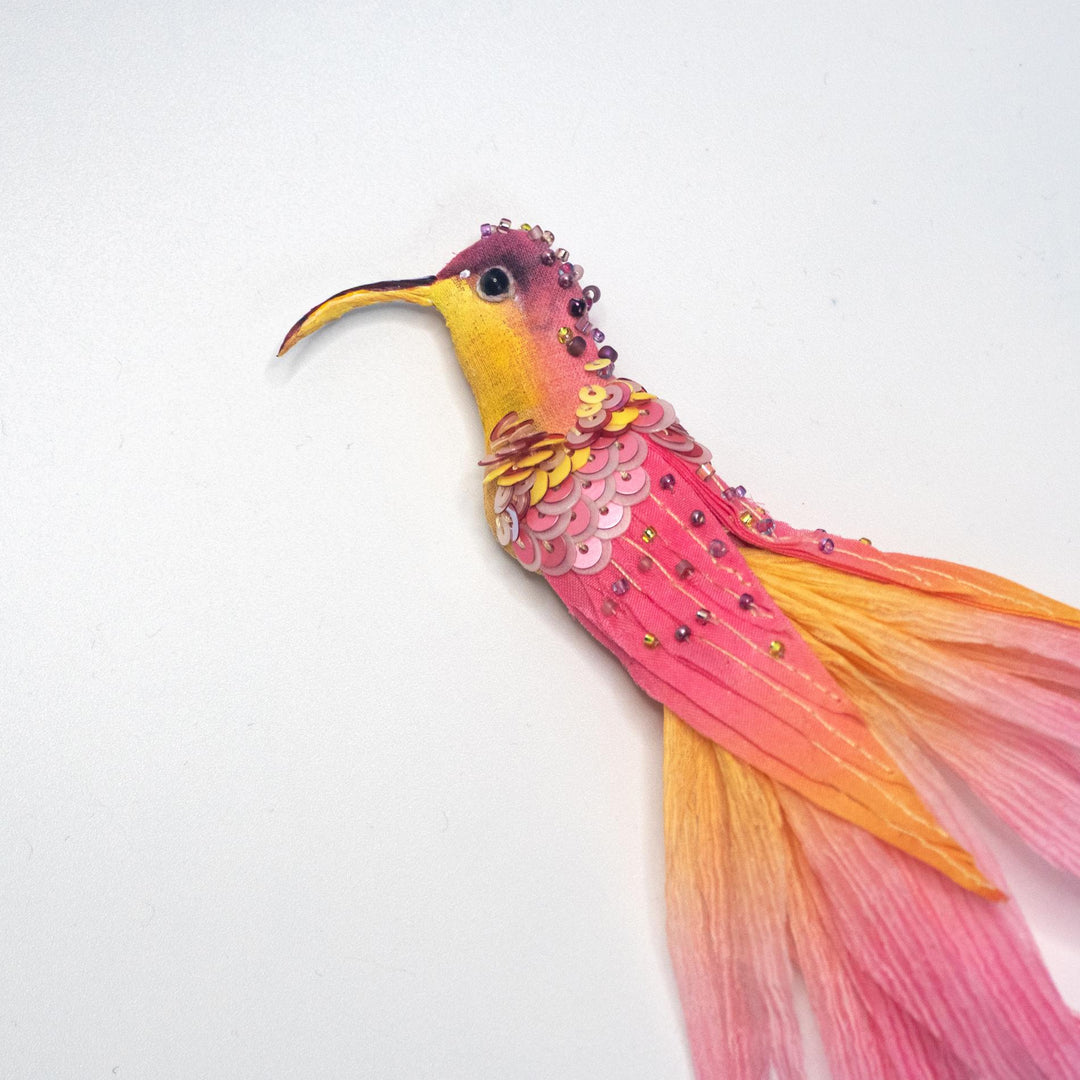 Close-up of the yellow and pink hummingbird brooch highlighting fine embroidery, sequins, and beadwork.