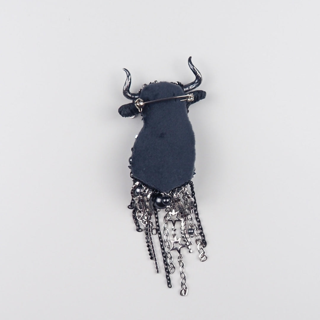 Back side of Taurus textile brooch showing soft black velvet backing and secure metal pin clasp with hanging chain elements