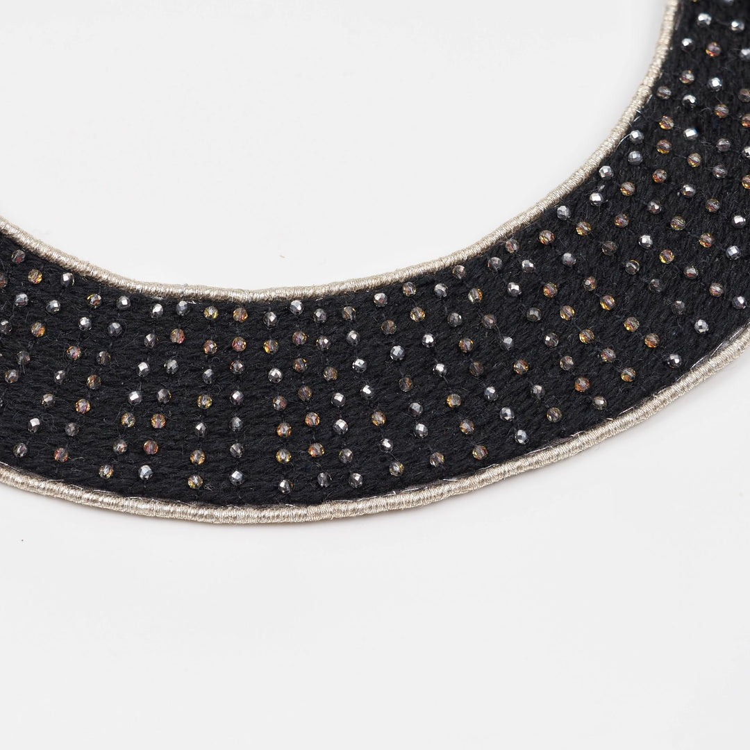 Close-up of a black collar necklace showing small faceted glass beads hand-set using a traditional pearl setting technique on a textile base.