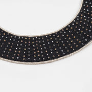 Close-up of a black collar necklace showing small faceted glass beads hand-set using a traditional pearl setting technique on a textile base.