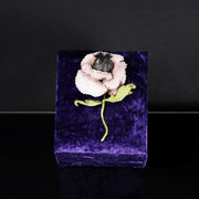 One-of-a-kind blush pink poppy brooch made of sequins and embroidered threads, displayed upright on a purple velvet stand