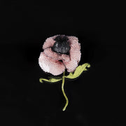 Close-up of handcrafted blush pink poppy brooch with sequin petals, embroidered leaves, and 3D structure, shown on a black background