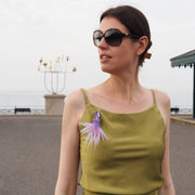 Close-up view of a handmade purple and white hummingbird brooch worn on a green dress. Detailed embroidery and beaded accents, crafted by UK textile artist