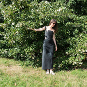 Woman wearing black embroidered corset with silver lining, styled outdoors against green foliage, showing full front silhouette