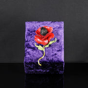 One-of-a-kind red poppy textile brooch with sequins and embroidered stem, displayed upright on a purple velvet stand