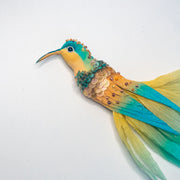 Side view of embroidered hummingbird brooch with teal head, golden body, and layered sequin embellishments.