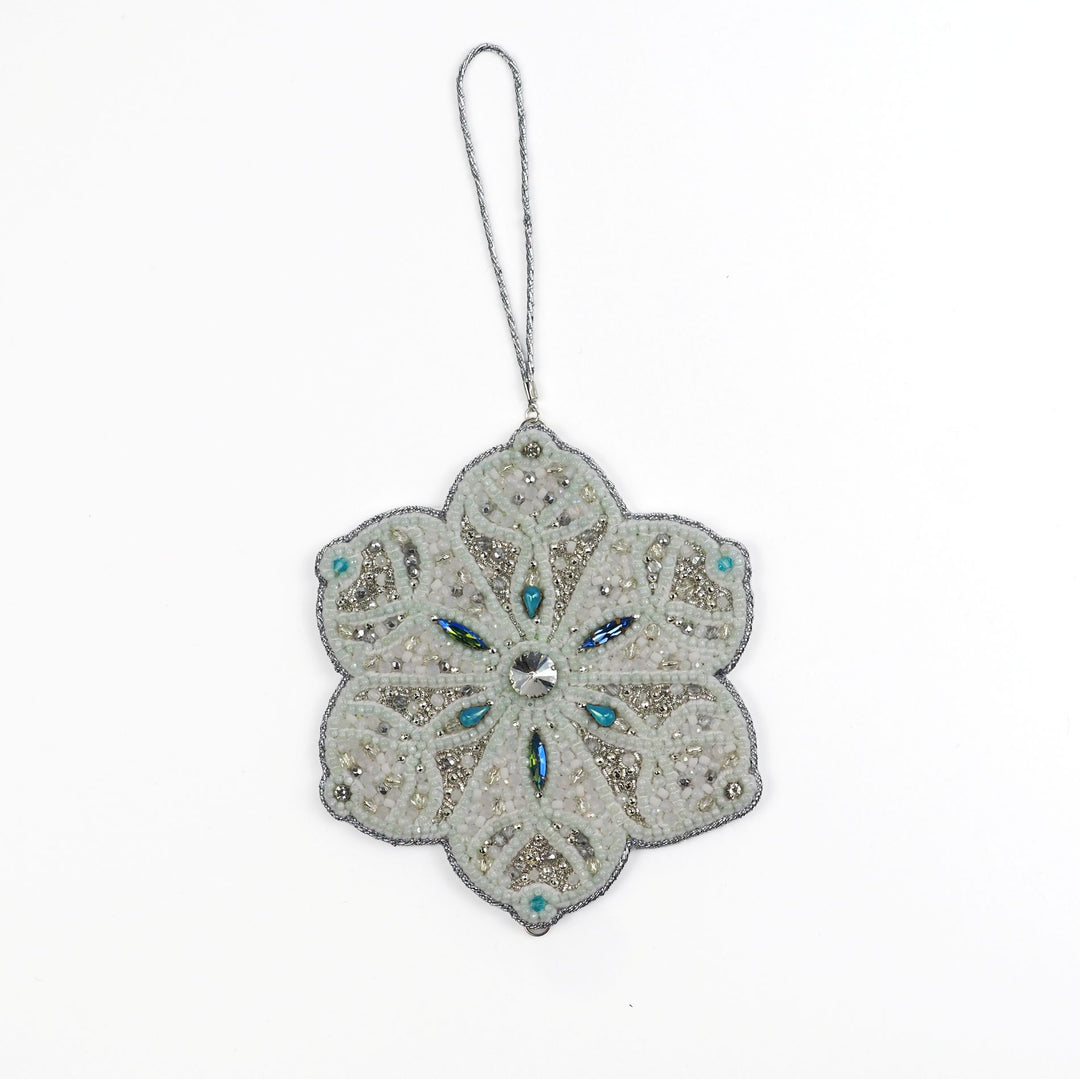 Full view of the Jewels of Winter Six-Pointed Snowflake Ornament by Ksenia Semirova. Hand-embroidered using the pearl-setting technique with white and silver beads, turquoise crystals, and a silver hanging cord.