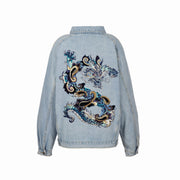 Back view of oversized light blue denim jacket featuring intricate dragon embroidery in blue, gold, and white threads, created with machine and hand embroidery techniques, on a white background.