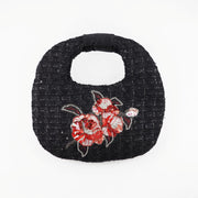 Hand-embroidered black tweed bag with red and silver camellia design, rounded shape, and maroon lining, designed by Ksenia Semirova