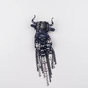 Close-up of handmade Taurus textile brooch featuring black embroidery, custom horns, glossy beads, and chain fringe with rhinestones